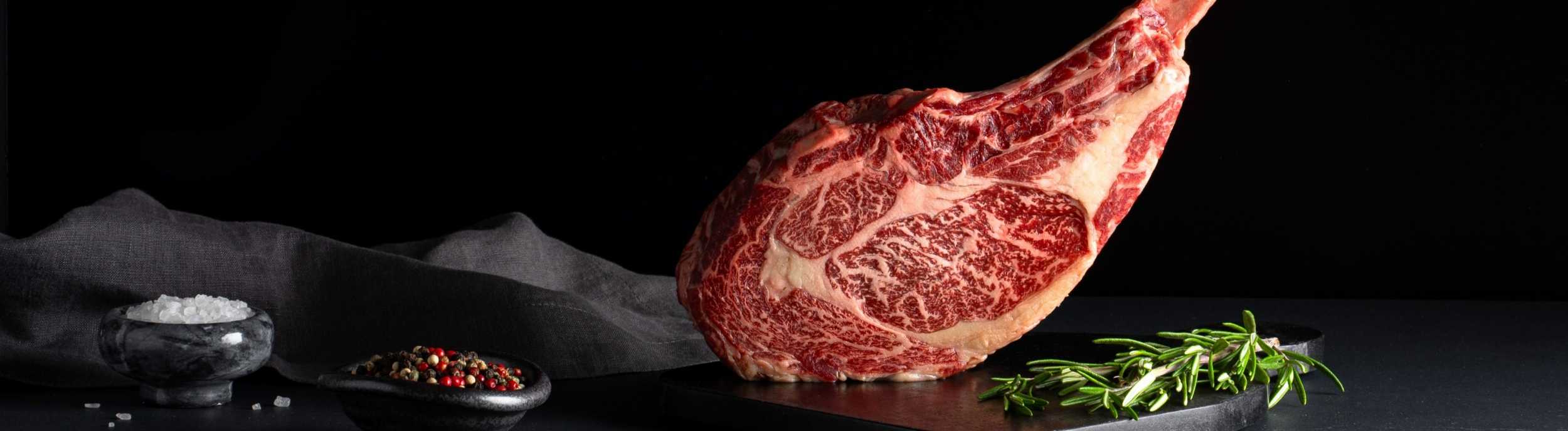 Raw tomahawk wagyu steak with long rib bone on display.