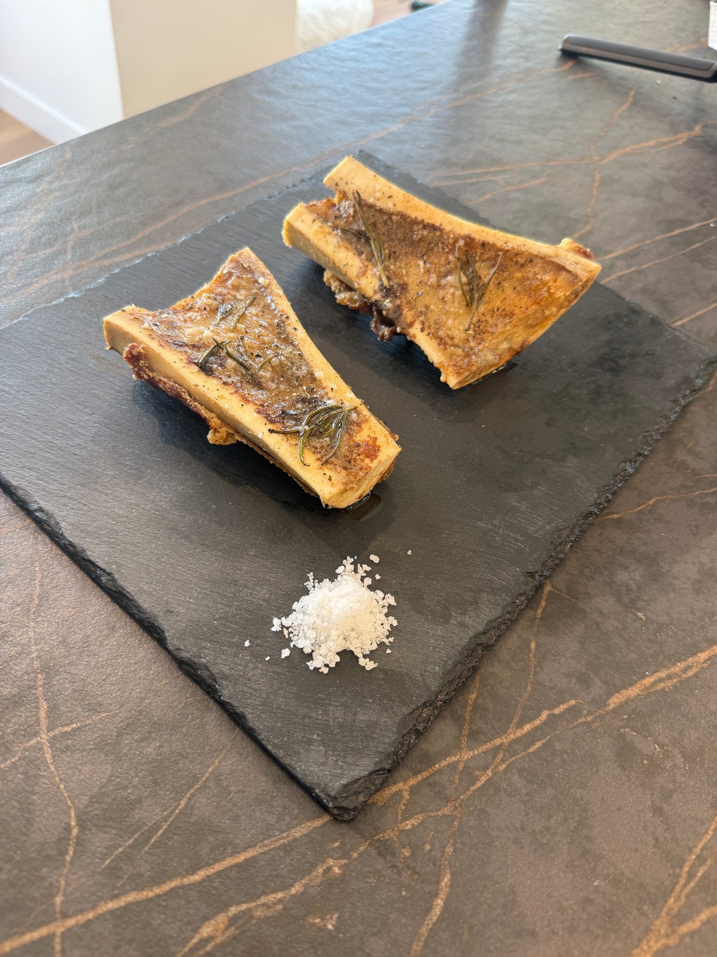 cooked American wagyu bone marrow with olive oil, rosemary and salt on a black board