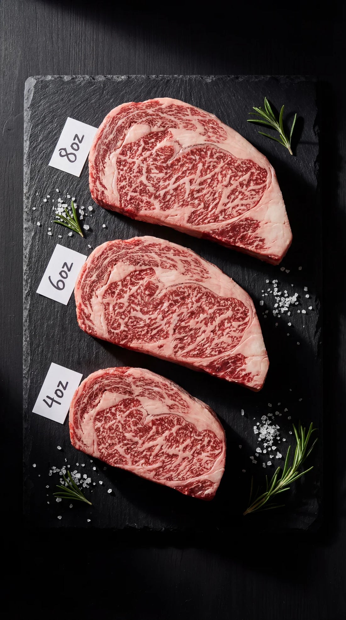 Three Japanese A5 wagyu ribeye steaks showing 4oz, 6oz, and 8oz portion sizes with intense marbling on black slate