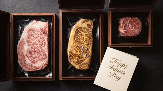 An elegant Father's Day gift arrangement of three Destination Wagyu Experience Boxes opened on dark slate, showing intensely marbled A5 Japanese and full blood Australian wagyu steaks