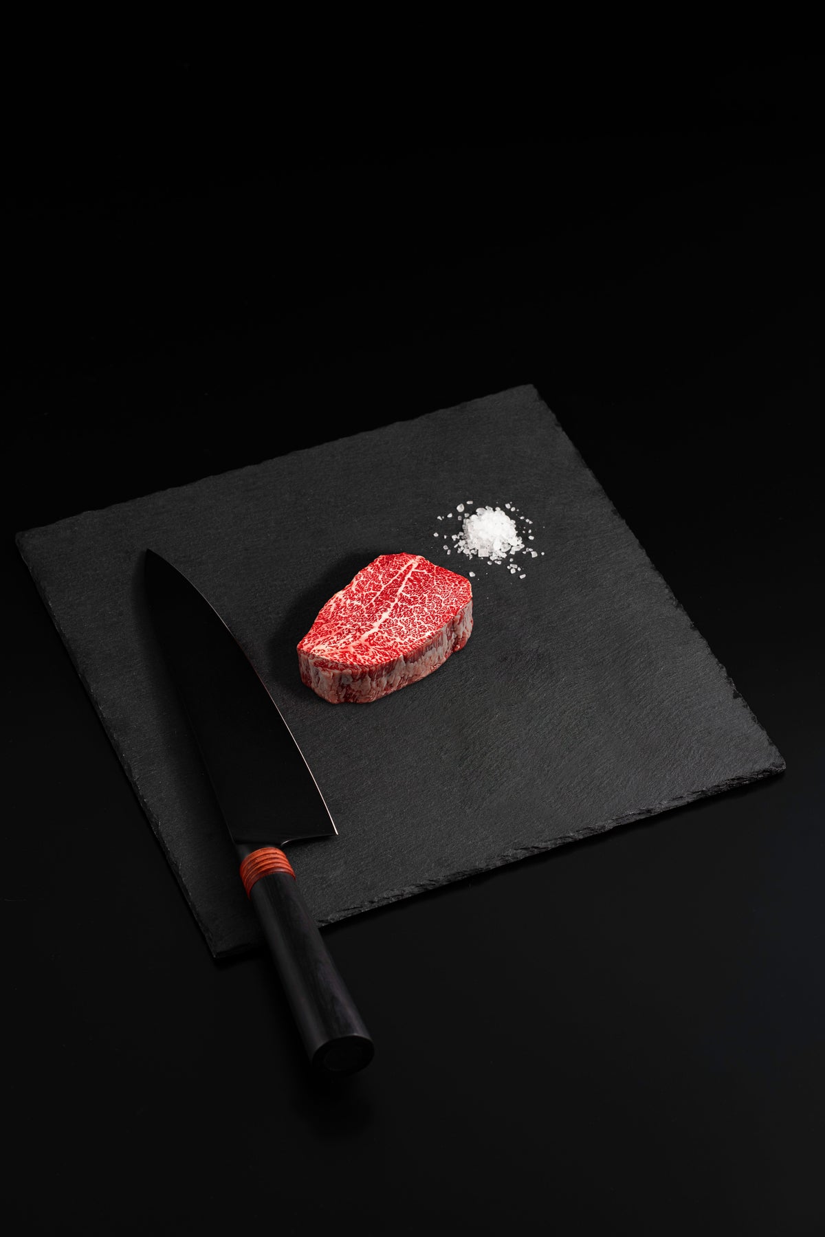 Japanese A5 Miyazaki Wagyu Petite Filet with sea salt and a black chef’s knife on a dark slate board