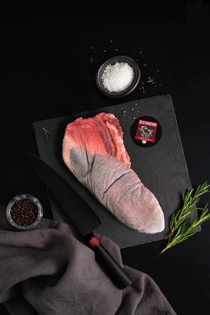 Australian Wagyu beef tongue on a black slate board with Destination Wagyu label, sea salt bowl, peppercorns, and rosemary on a dark background