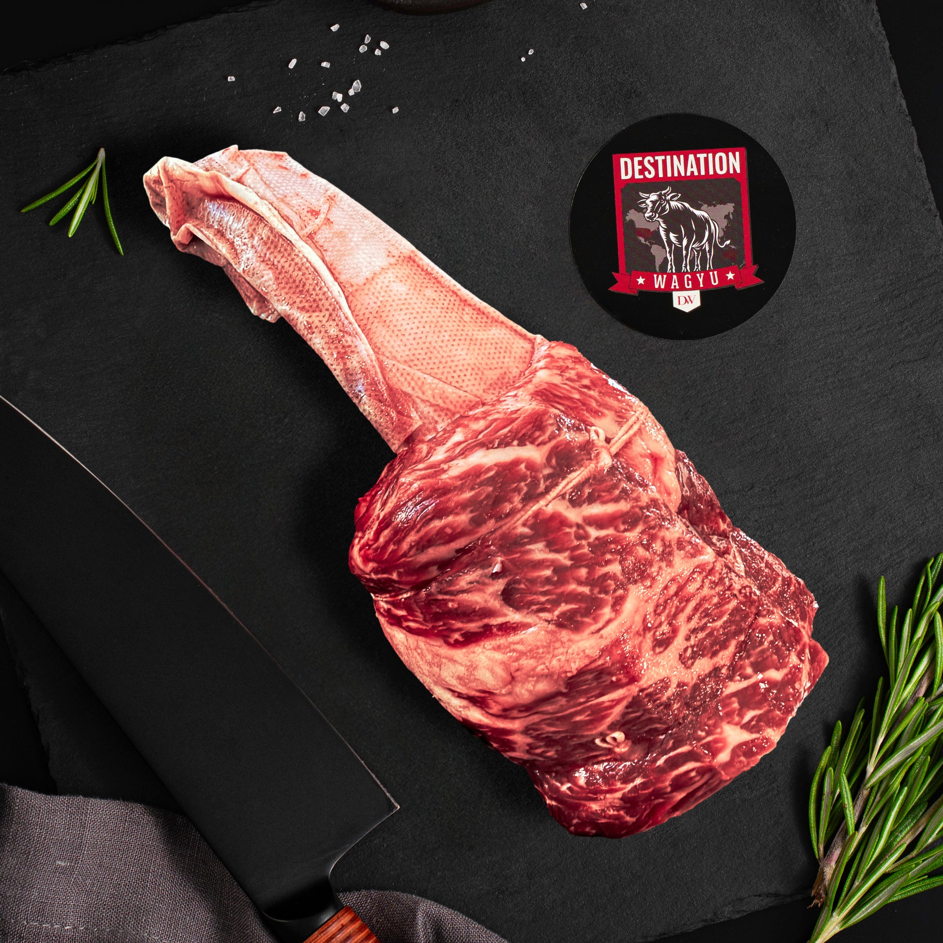 An Australian wagyu Short Rib Tomahawk on a slate black board with knife and destination wagyu logo