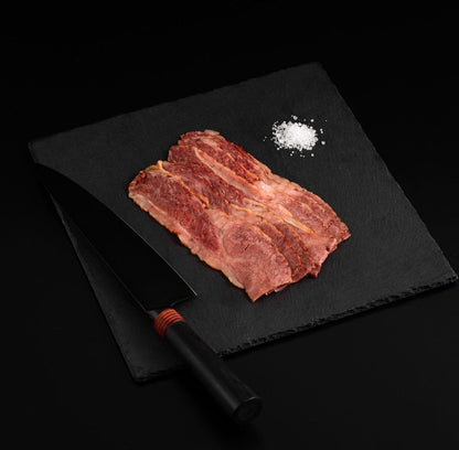 An Australian Wagyu Beef Bacon with salt and chef's knife on a black slate, isolated on black background.