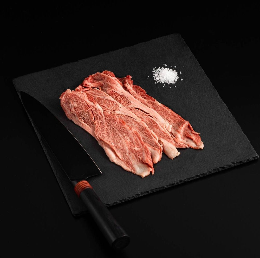 A Japanese A5 Wagyu Sliced Chuck Roll with salt and chef's knife on a black slate, isolated on black background.