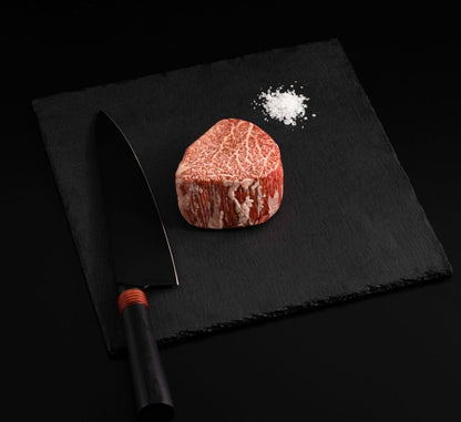 A Japanese A5 Wagyu Miyazaki Filet Steak with salt and chef's knife on a black slate, isolated on black background.