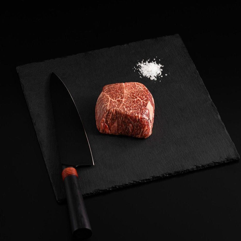 A Japanese A5 Wagyu Top Sirloin with salt and chef's knife on a black slate, isolated on black background.