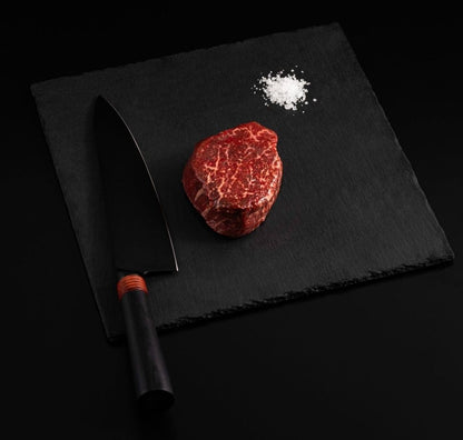 An Australian Wagyu Fullblood Jade Filet Mignon with salt and chef's knife on a black slate, isolated on black background.