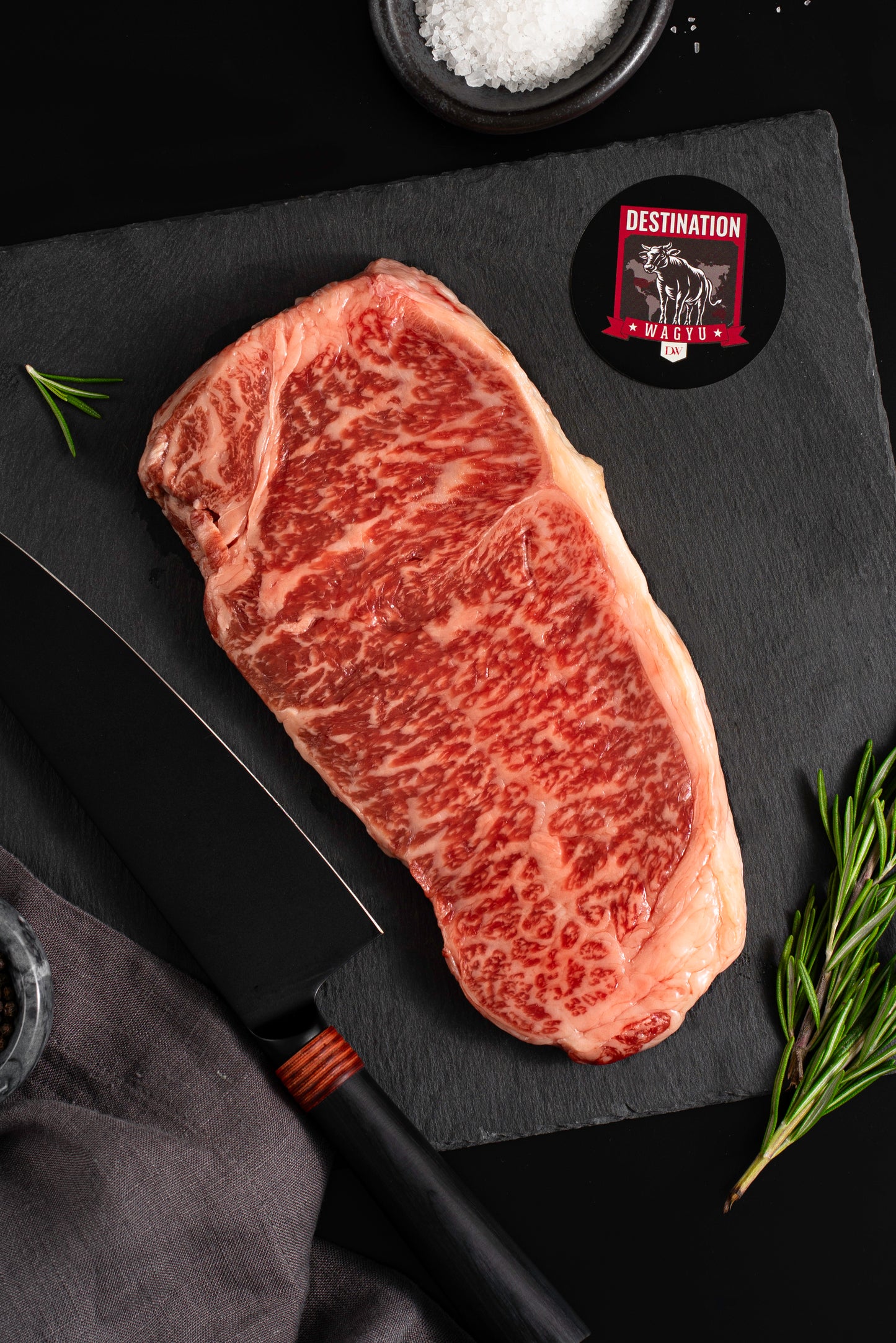 A 16oz Japanese a5 wagyu striploin steak on a black board with salt and knife 
