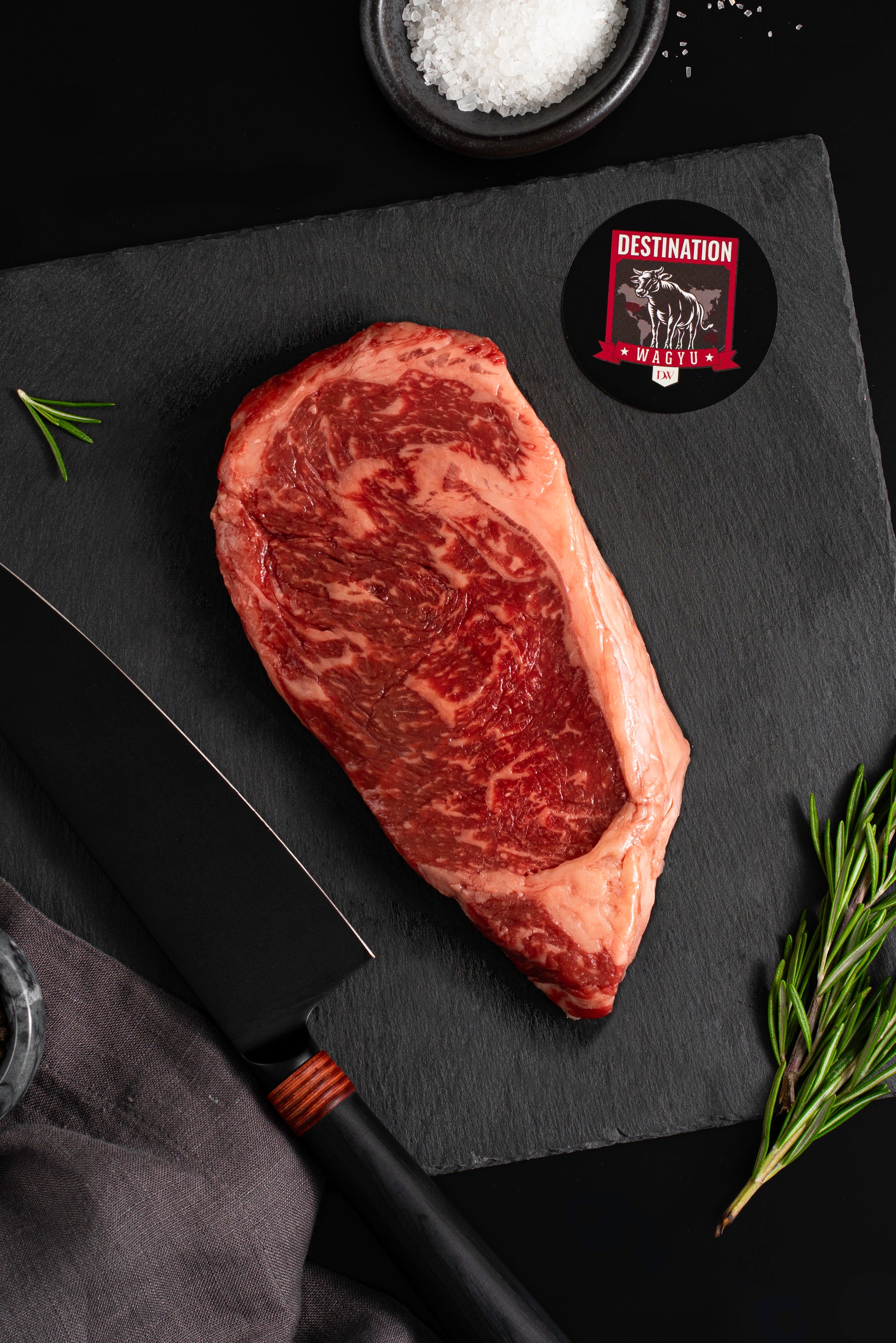 An american wagyu striploin steak on a black board with knife and salt