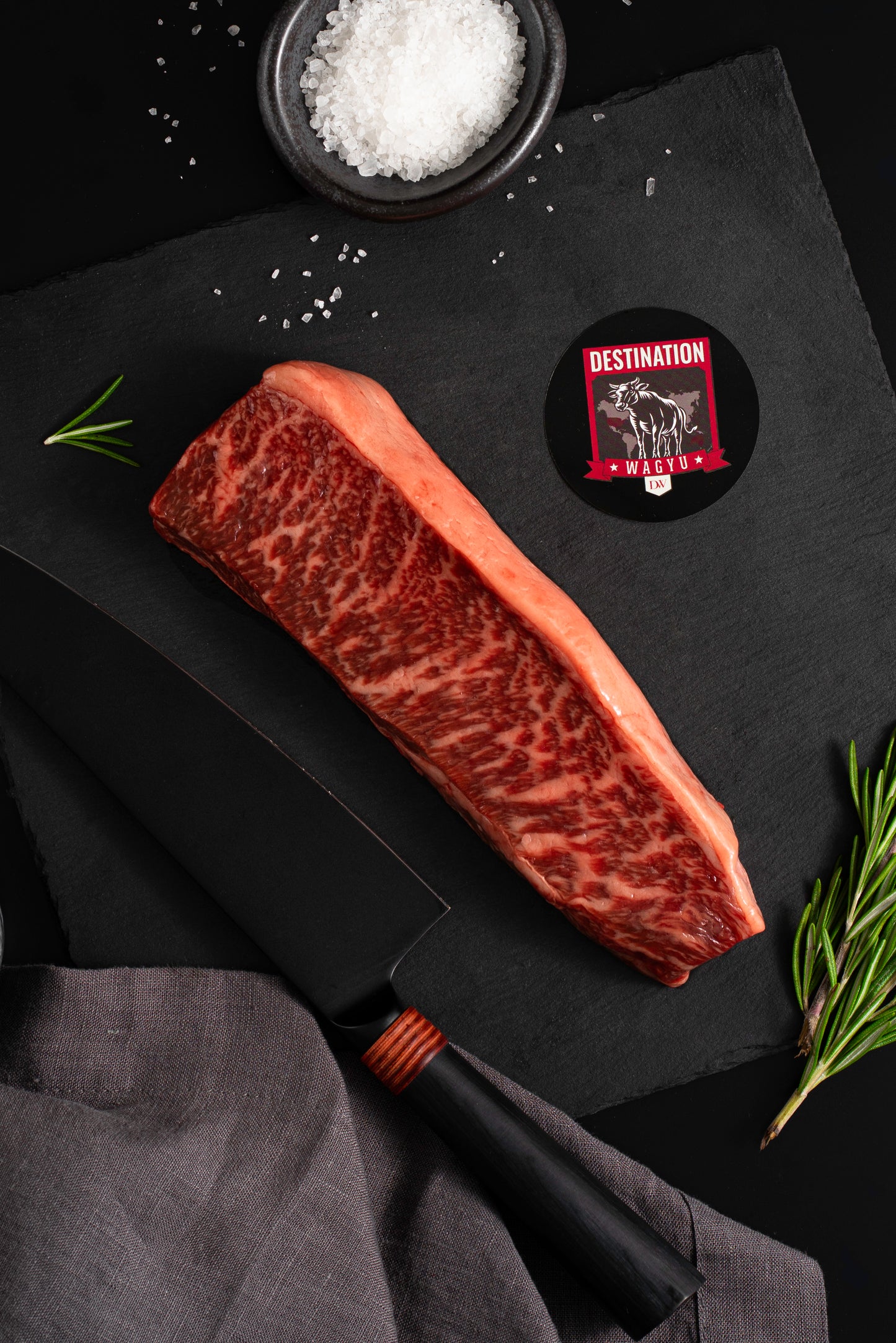 An australian wagyu picanha steak in 12oz size on a slate black board with salt and a knife