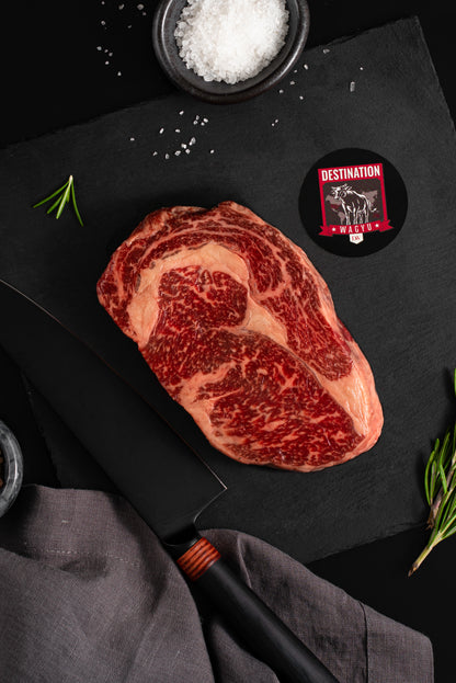 An Australian wagyu ribeye steak in 16oz size on a black board with salt and knife 