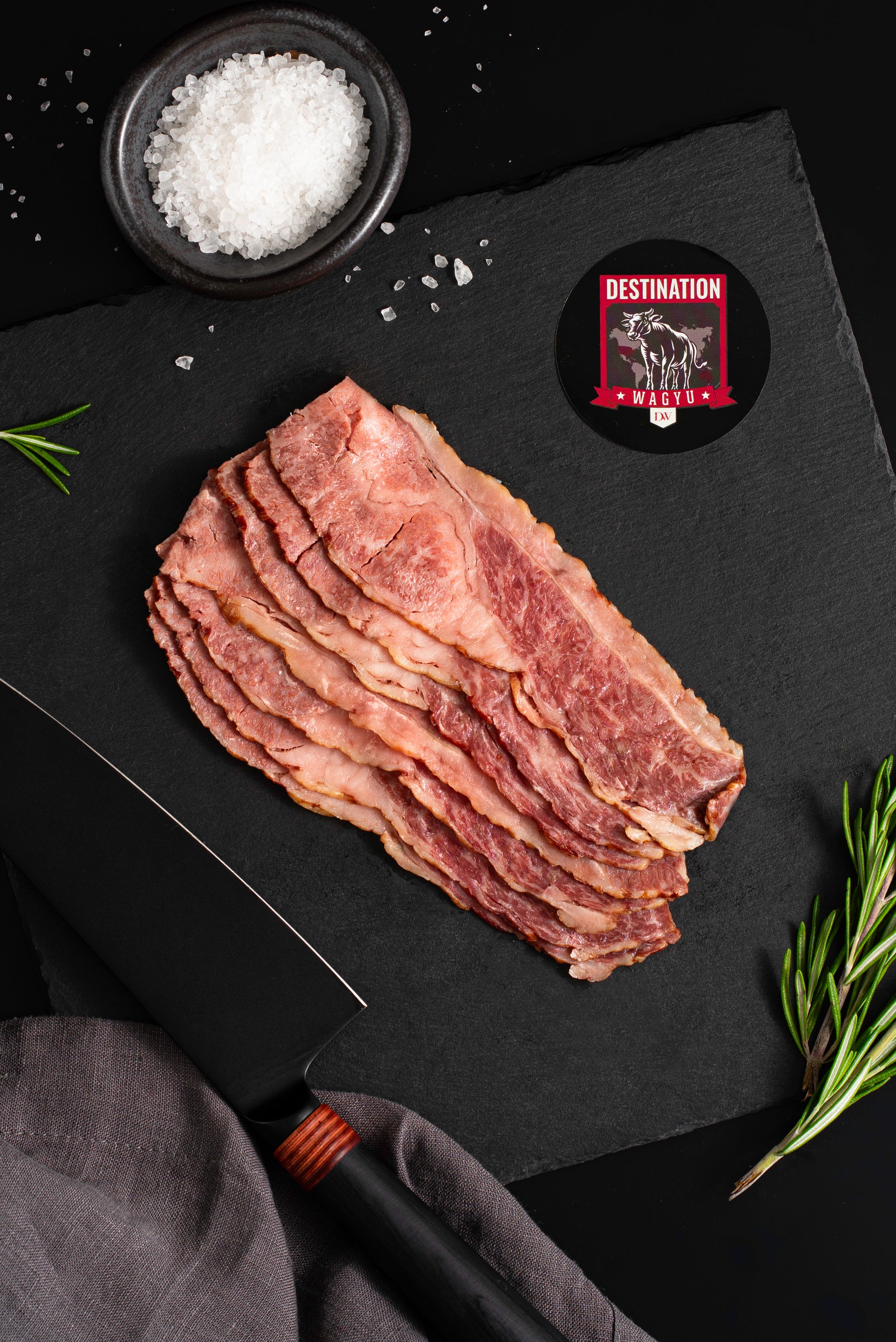 Australian wagyu beef bacon in 16oz size on a black board with salt and a knife