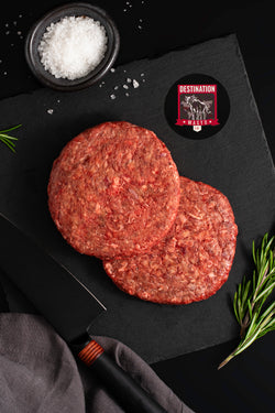 Two raw australian wagyu burger patties on a black board with salt and knife