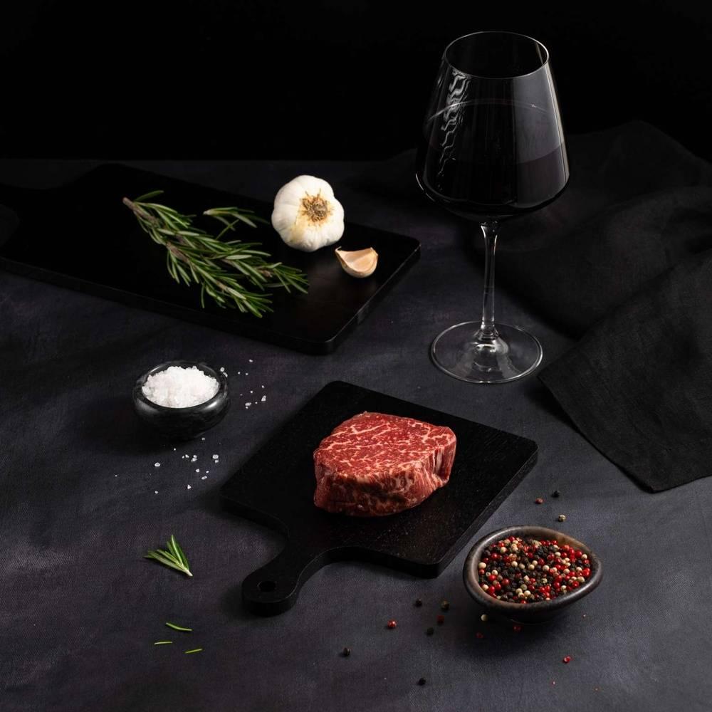 An Australian Wagyu Fullblood Jade Filet Mignon with salt and chef's knife on a black slate, isolated on black background.