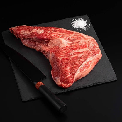 Raw marbled American Wagyu Masami Tri Tip with salt and chef's knife on a black slate, isolated on black background.