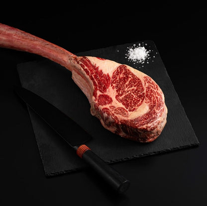 An Australian Wagyu Tomahawk Steak with salt and chef's knife on a black slate, isolated on black background.