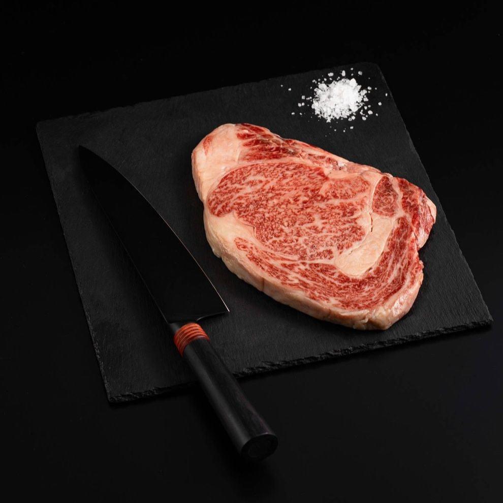 A Japanese A5 Wagyu Miyazaki Ribeye Steak with salt and chef's knife on a black slate, isolated on black background.