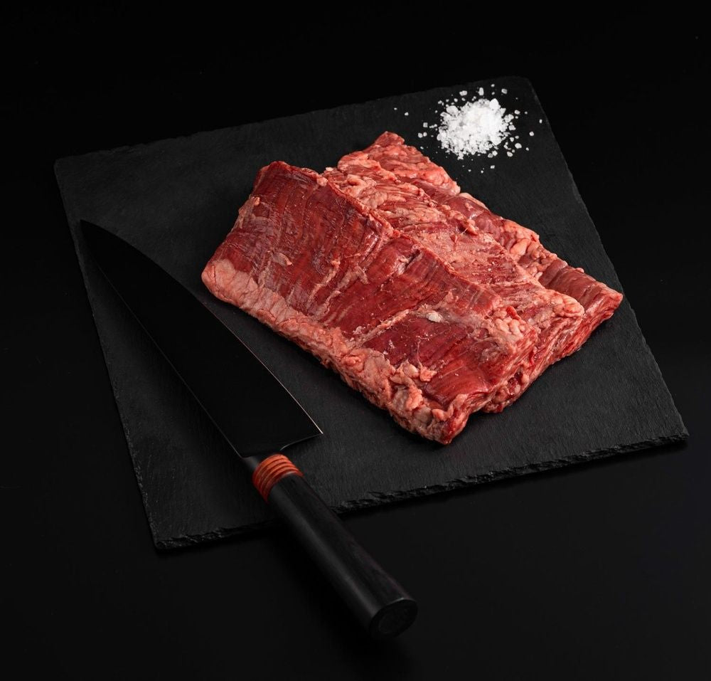 Australian Wagyu Outside Skirt Steak with salt and chef's knife on a black slate, isolated on black background.