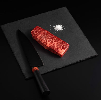 An Australian Wagyu Full Blood Denver Steak with salt and chef's knife on a black slate, isolated on black background.