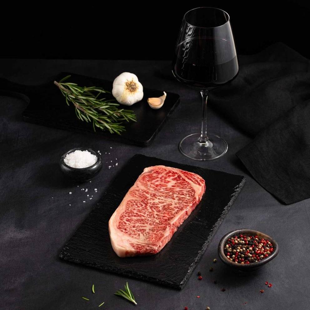 A Japanese A5 Wagyu Striploin Miyazaki Steak with salt and chef's knife on a black slate, isolated on black background.