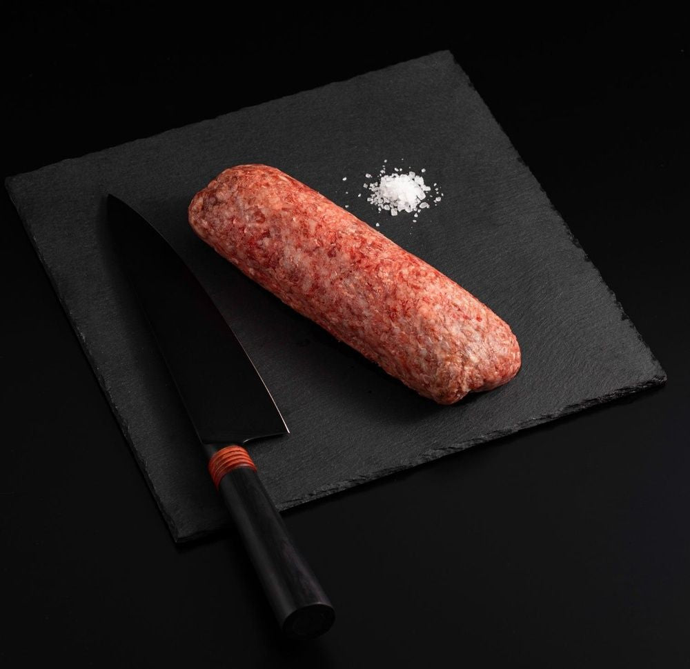 A slab of Japanese A5 Wagyu Ground Beef with salt and chef's knife on a black slate, isolated on black background.