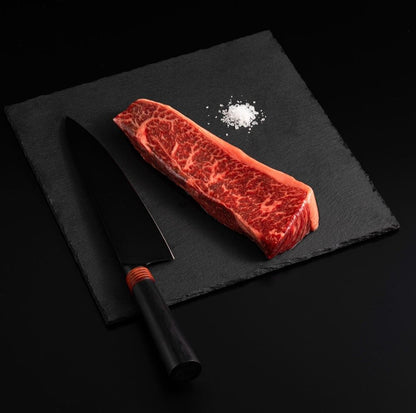 An Australian Wagyu Top Coulotte Picanha Steak with salt and chef's knife on a black slate, isolated on black background.