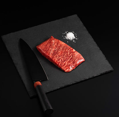 An Australian Wagyu Full Blood Flat Iron Steak with salt and chef's knife on a black slate, isolated on black background.