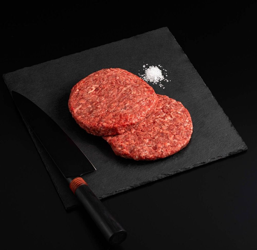 Two Australian Wagyu Beef Patties with salt and chef's knife on a black slate, isolated on black background.