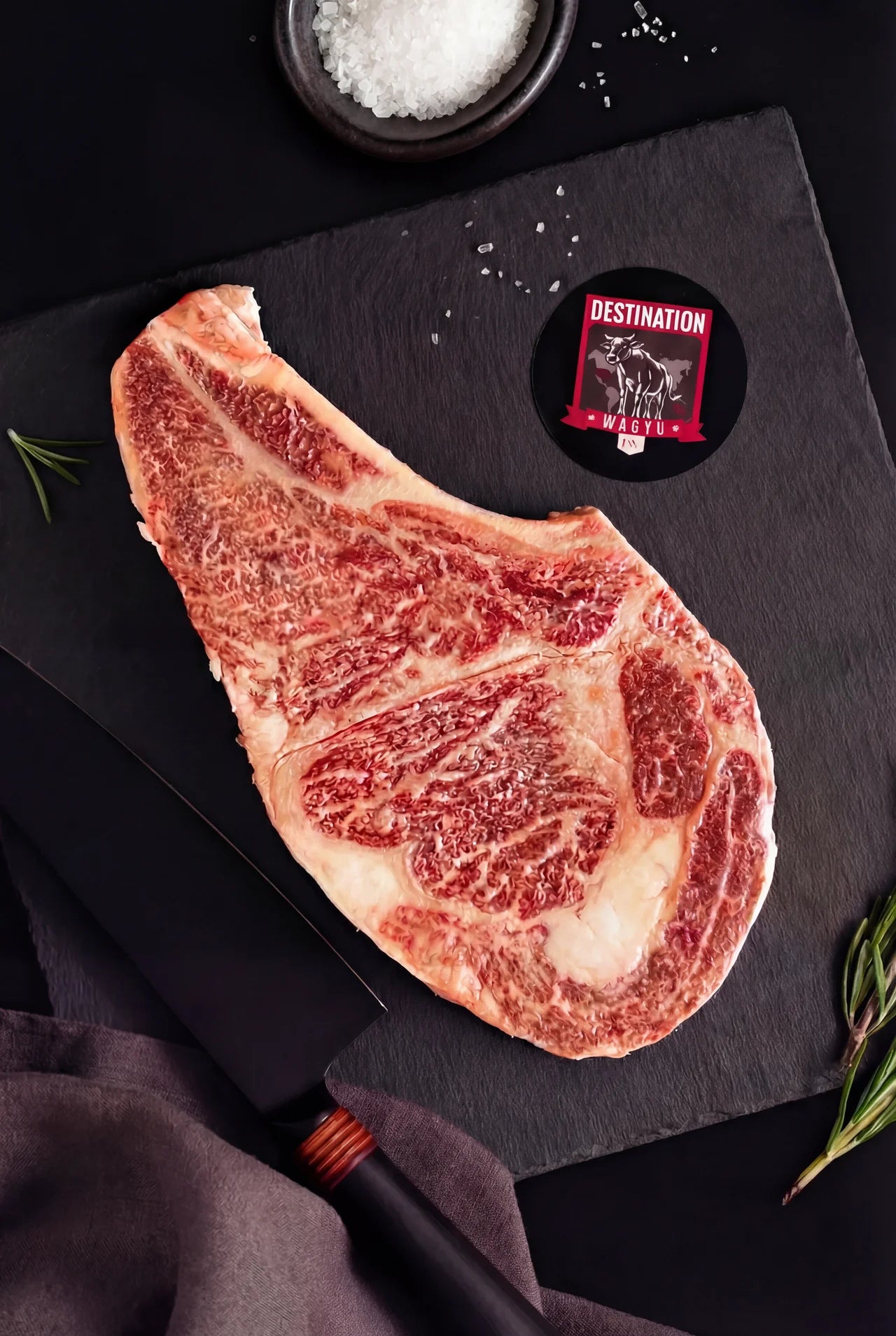 An australian wagyu bone in ribeye steak from stone-axe farm on a black slate board with knife and salt. 